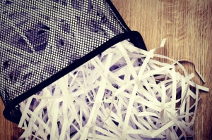 Strips of destroyed paper from shredder in trash can on wooden background